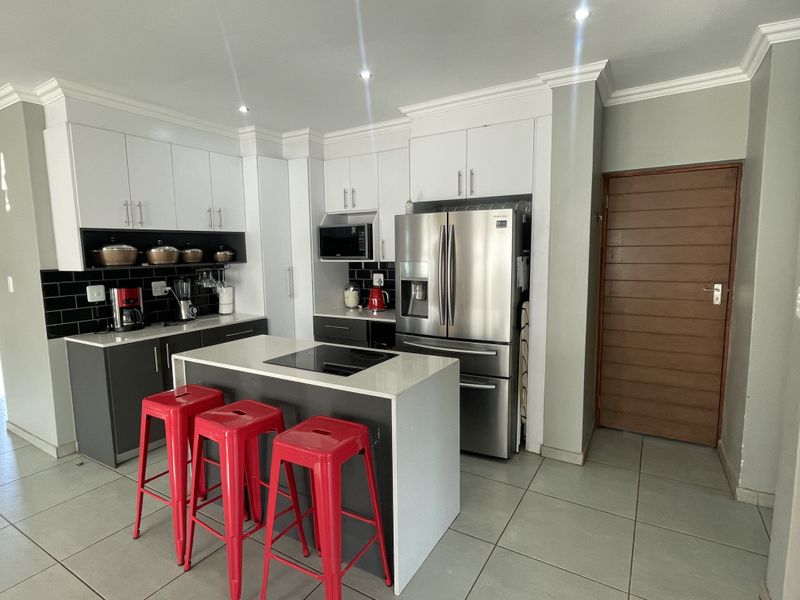 Modern kitchen featuring white and grey cabinetry, stone countertops, a central island with a cooktop, and stylish black subway tile backsplash.