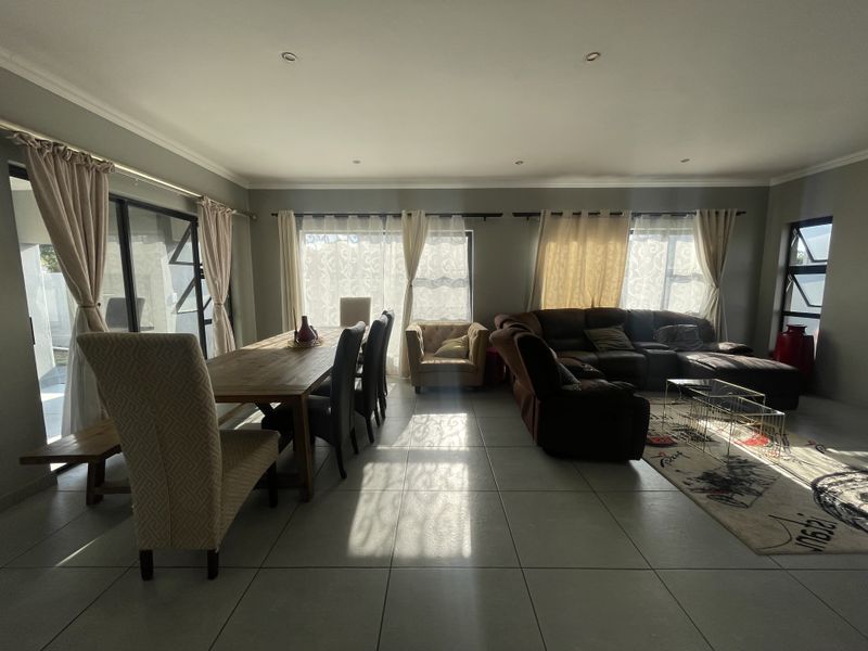Spacious open-plan living and dining area featuring large windows, sliding glass doors, tiled flooring, and recessed downlighting.