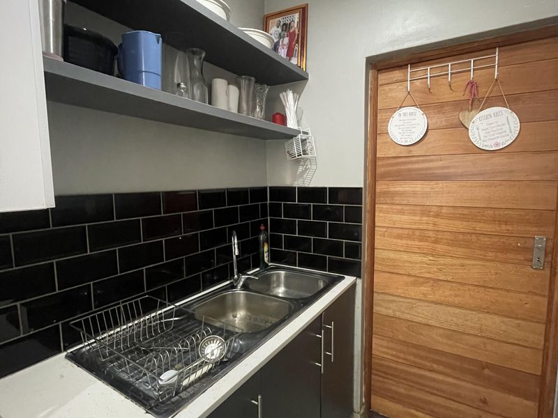 A functional scullery featuring a double bowl stainless steel sink, black subway tile backsplash, quartz countertops, and ample built-in cabinetry with floating shelves.