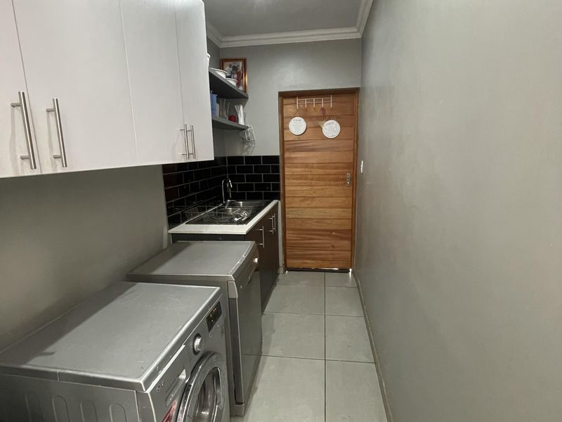 A functional laundry area featuring built-in cabinetry, a sink with a tiled backsplash, and neutral floor tiles.
