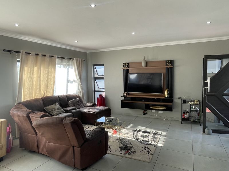 A well-maintained living room featuring tiled flooring, recessed downlighting, and a modern built-in media unit with integrated shelving.