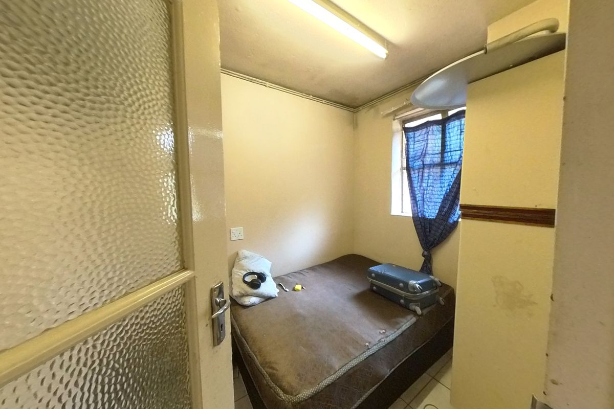 A compact bedroom featuring a textured glass door and basic lighting, currently requiring cosmetic updates and wall repairs to improve its overall condition.