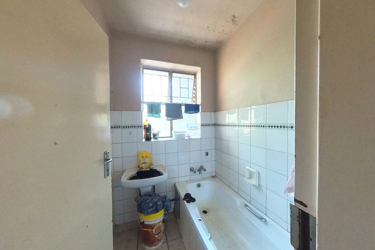 A dated bathroom featuring a bathtub, wall-mounted basin, and tiled walls, requiring cosmetic updates and maintenance to the ceiling and finishes.