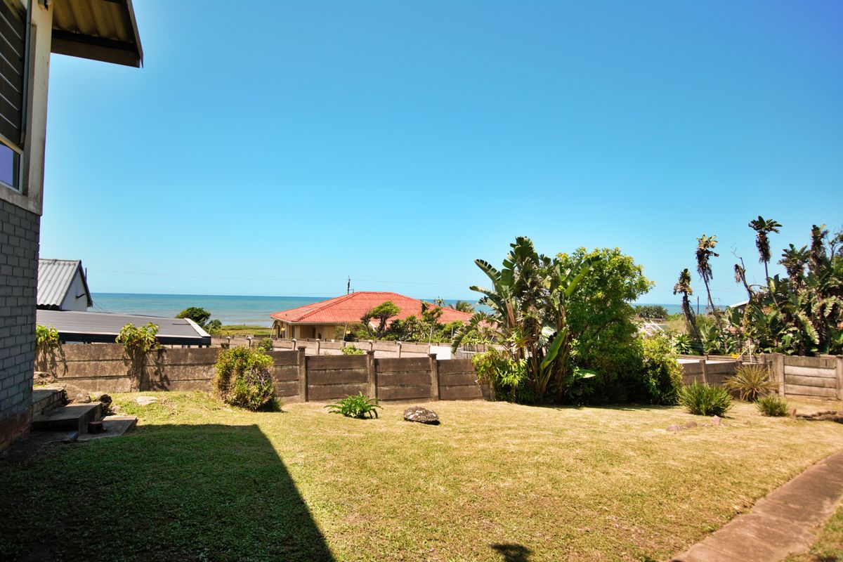 A rear garden view featuring a lawn, paved walkway, and precast concrete boundary wall with a distant ocean view.