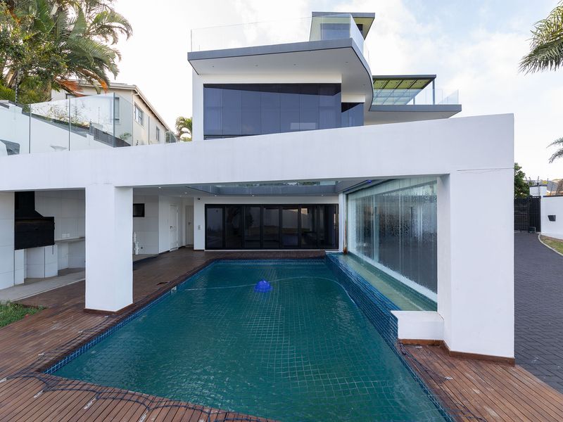 Modern multi-level home featuring a sleek swimming pool with a built-in water feature, timber decking, and expansive glass balustrades for a contemporary outdoor living experience.