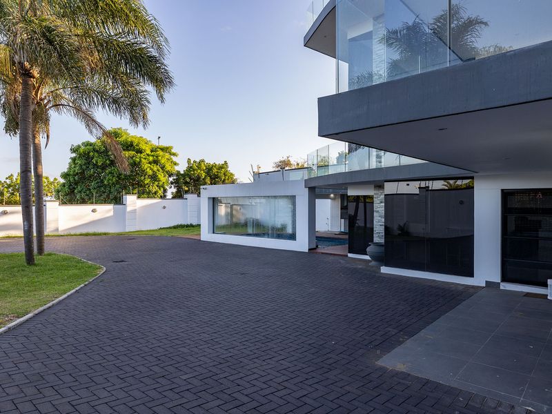 Modern architectural home exterior featuring a paved driveway, glass balcony balustrades, and secure perimeter walling with electric fencing.