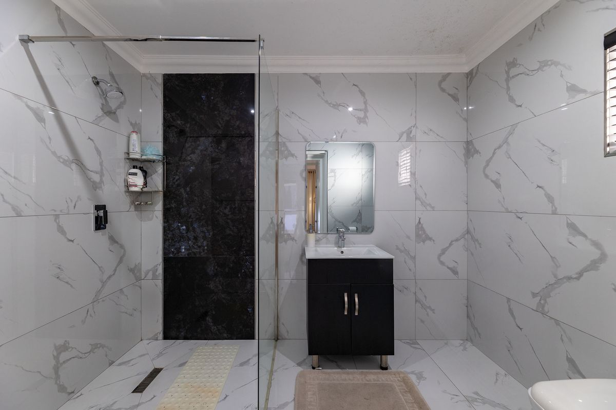 Modern bathroom featuring marble-look wall tiles, a spacious walk-in shower with a glass screen, and a sleek vanity unit with a basin.
