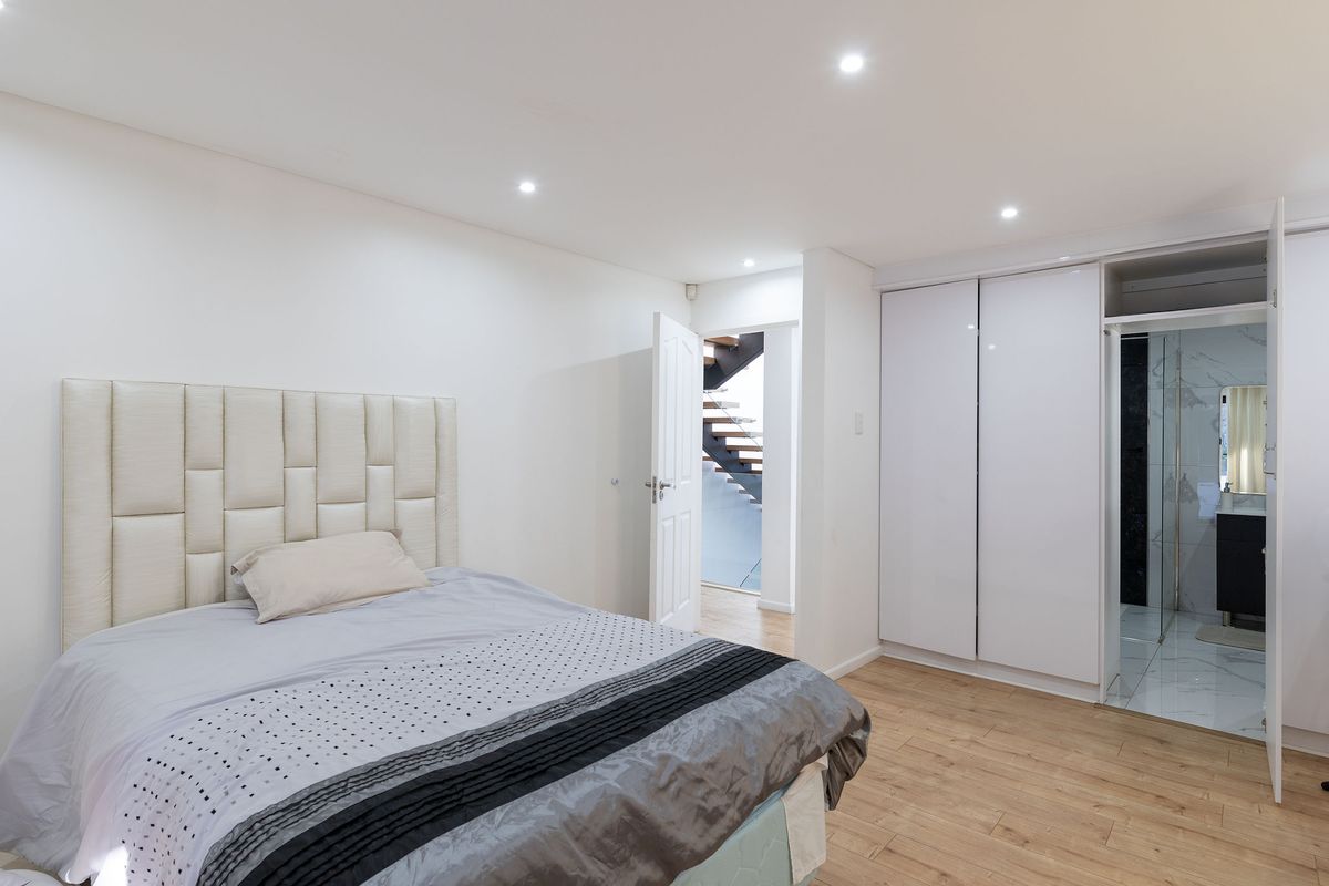 A modern bedroom featuring laminate flooring, recessed downlights, and built-in cupboards with direct access to an en-suite bathroom.