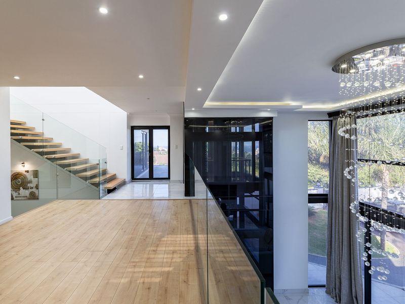 A modern, spacious landing area featuring a floating staircase with glass balustrades, high-end finishes, and a striking crystal chandelier overlooking the lower level.