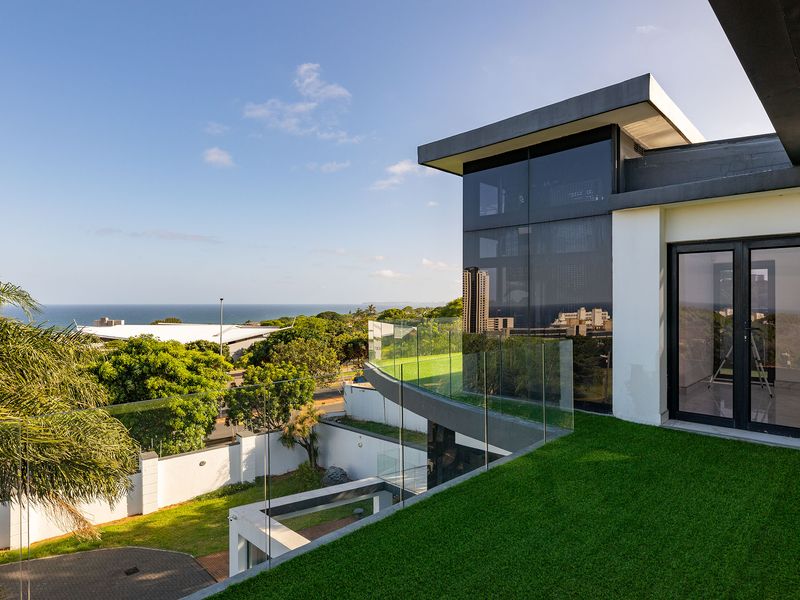 Modern balcony featuring a glass balustrade and artificial turf, offering expansive views of the surrounding landscape and coastline.