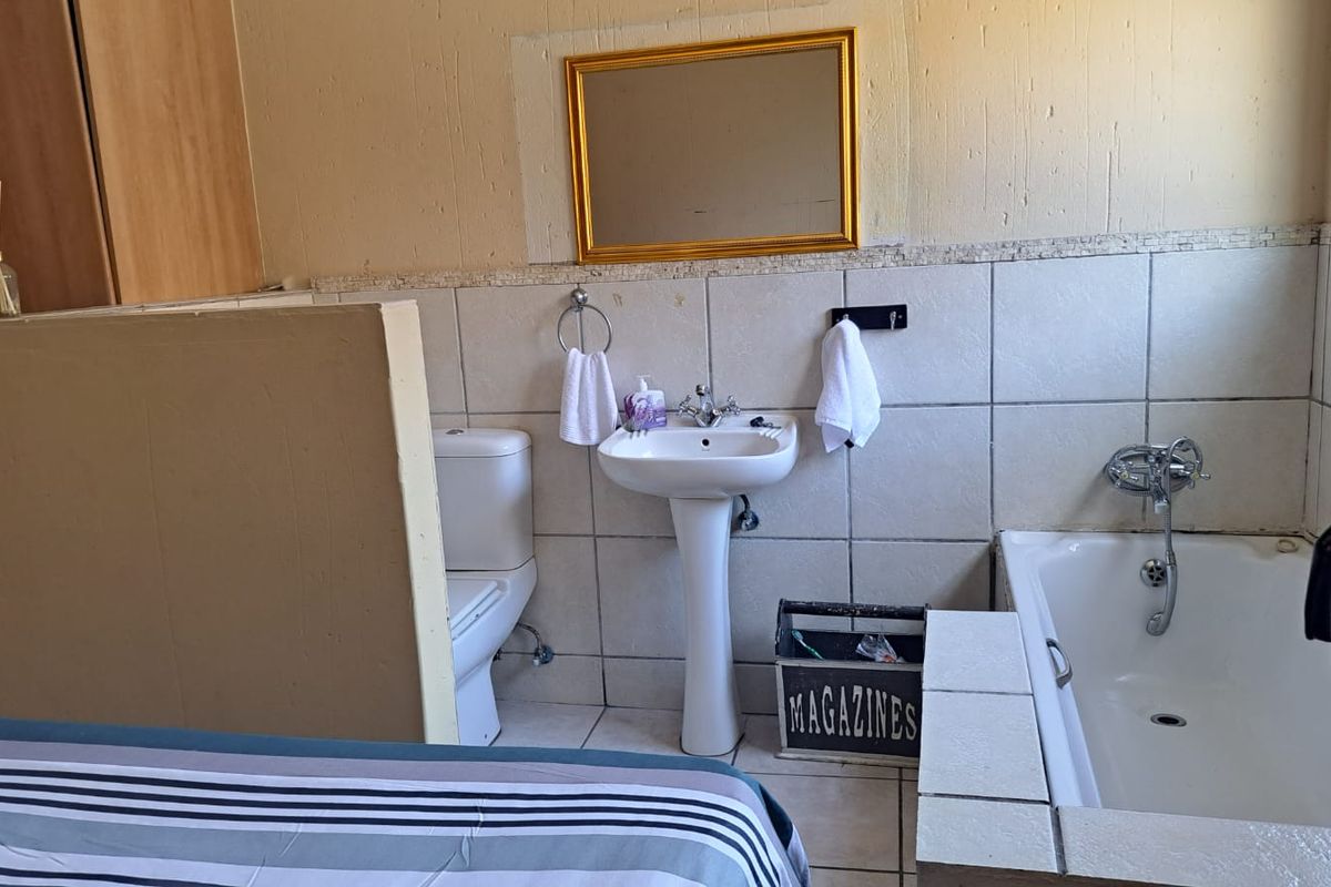 A functional bathroom featuring a pedestal basin, a built-in bathtub, and a toilet, finished with neutral wall tiling.