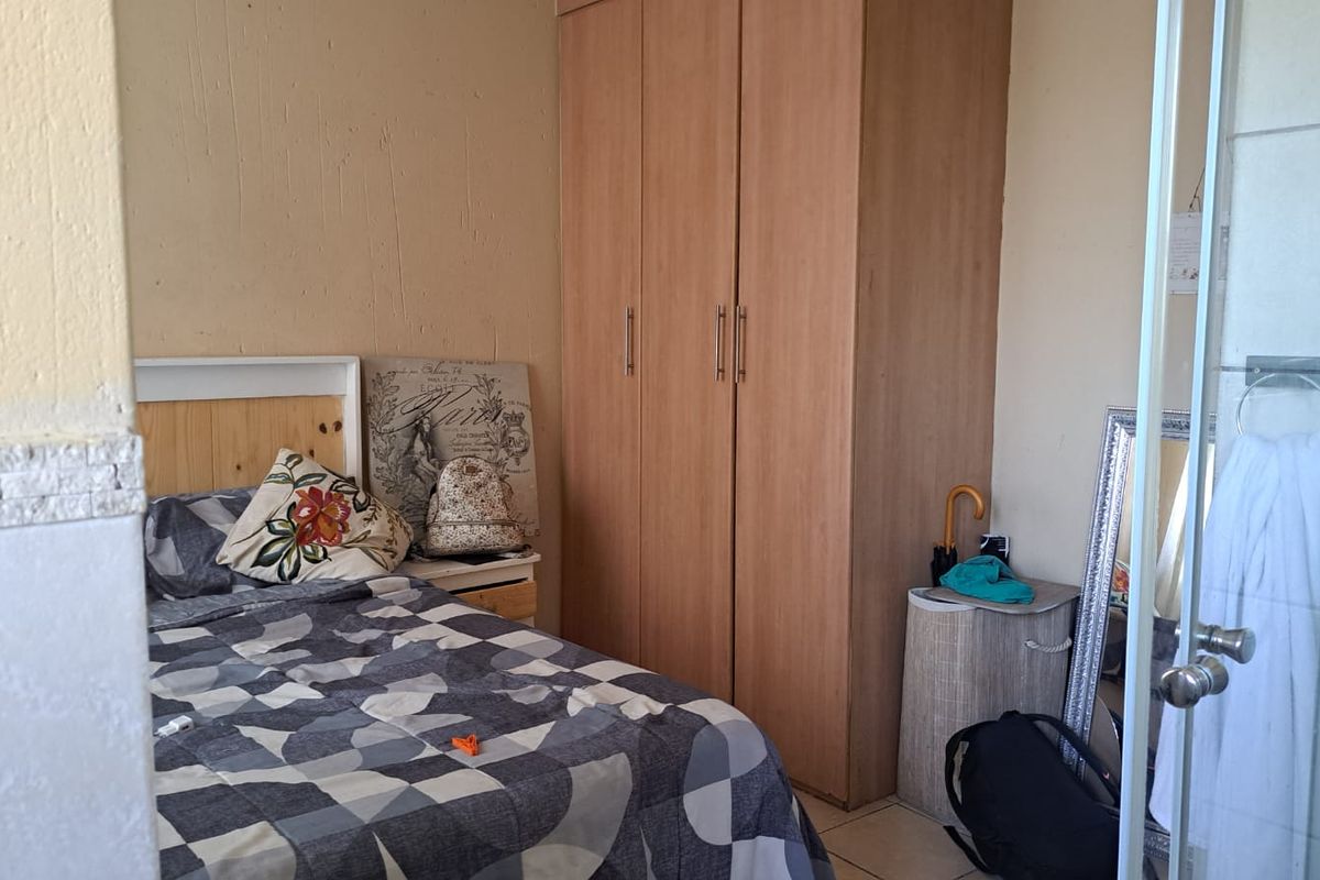 A bedroom featuring a built-in wooden wardrobe and tiled flooring, with direct access to an adjacent bathroom area.