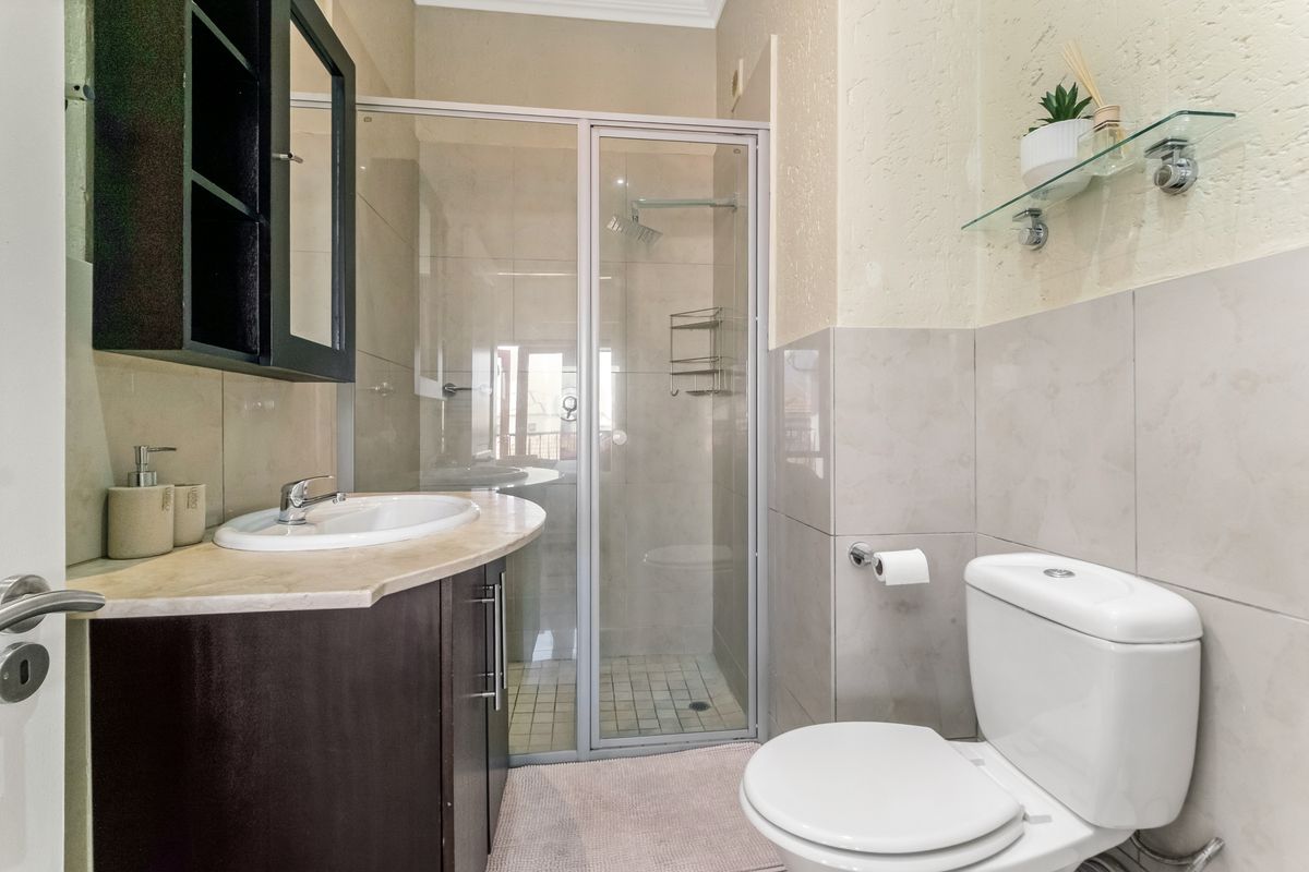 A compact, well-maintained bathroom featuring a vanity with integrated basin, a glass-enclosed shower, and a standard toilet with neutral wall tiling.