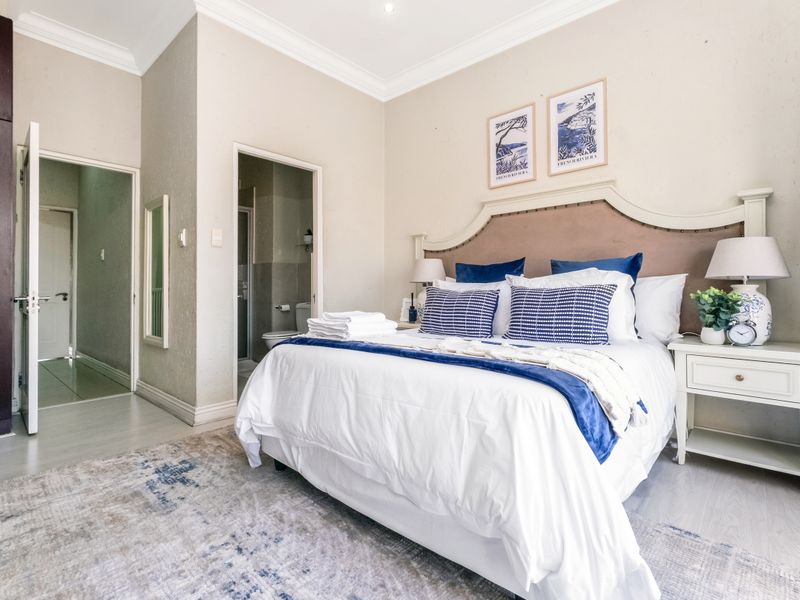 A well-maintained bedroom featuring laminate flooring, built-in cupboards, and an adjoining en-suite bathroom with neutral finishes.