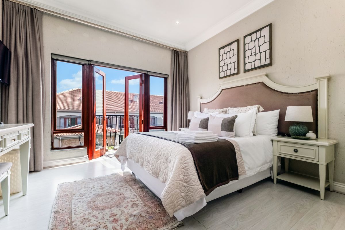 A well-maintained bedroom featuring crown molding, recessed lighting, and double doors opening to a balcony, providing ample natural light and a pleasant outlook.