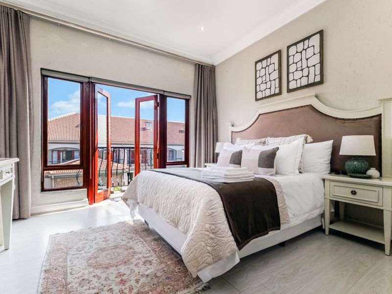 A well-maintained bedroom featuring crown molding, recessed lighting, and double doors opening to a balcony, providing ample natural light and a pleasant outlook.