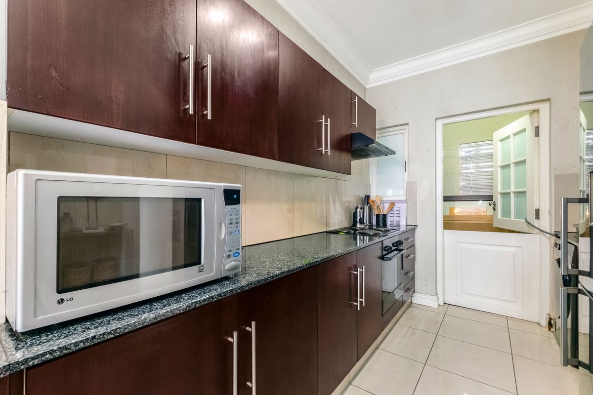 A functional kitchen featuring dark wood cabinetry, granite countertops, built-in oven, extractor fan, and tiled flooring with a classic stable door entrance.