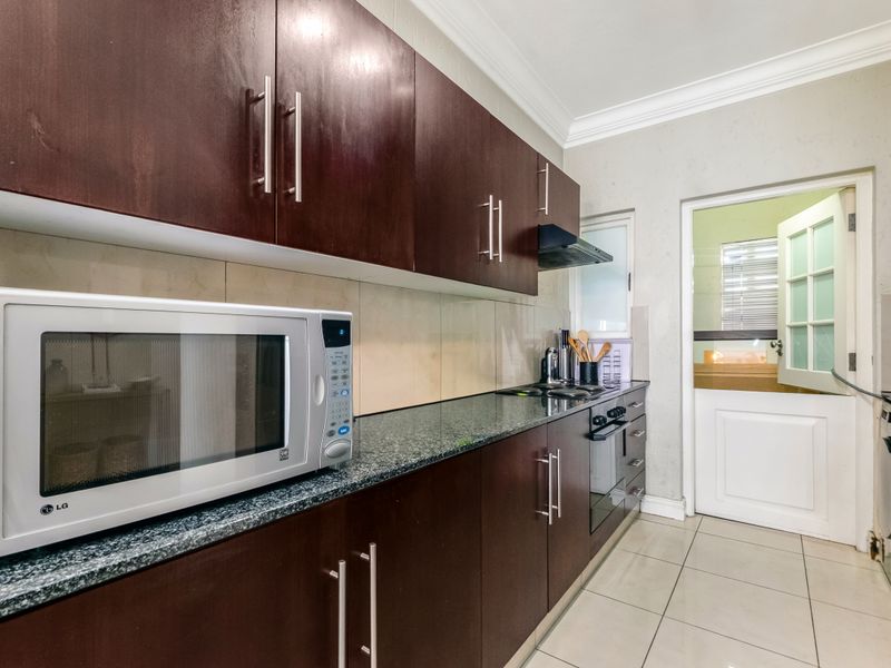 A functional kitchen featuring dark wood cabinetry, granite countertops, built-in oven, extractor fan, and tiled flooring with a classic stable door entrance.