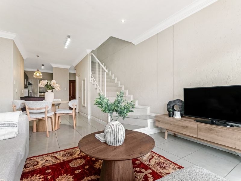 Open-plan living and dining area featuring tiled floors, a staircase with white balustrades, and a modern kitchen visible in the background.