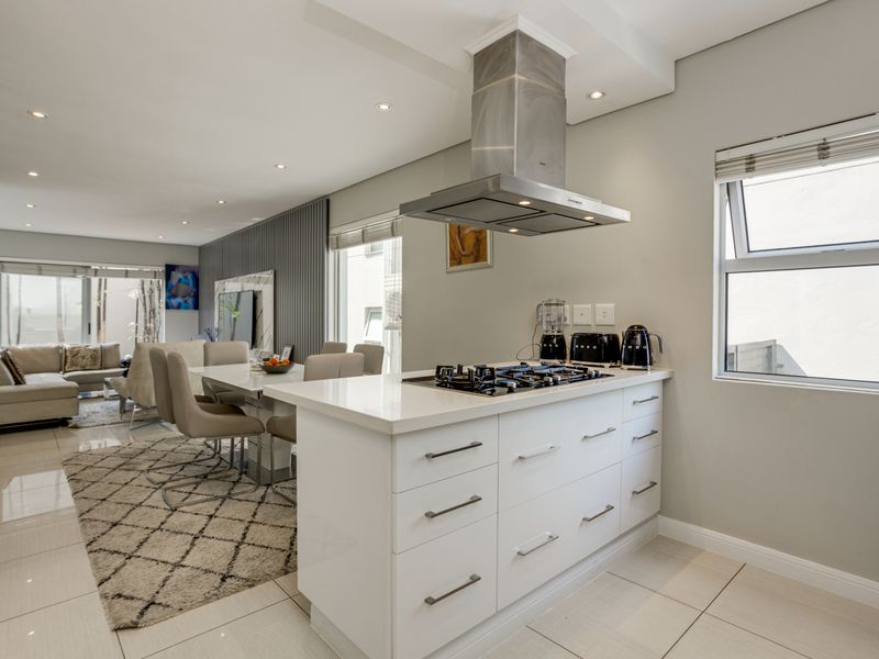 Modern open-plan kitchen featuring a central island with a gas hob and stainless steel extractor fan, seamlessly flowing into the adjacent dining and living area.