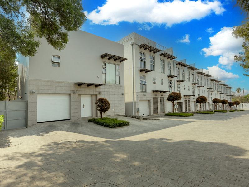 A modern multi-story townhouse complex featuring paved driveway access, integrated garages, and contemporary architectural detailing with stone cladding accents.