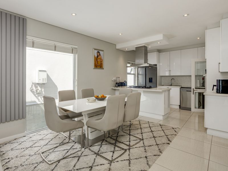 Modern open-plan kitchen and dining area featuring sleek white cabinetry, integrated appliances, tiled flooring, and direct access to an outdoor patio space.