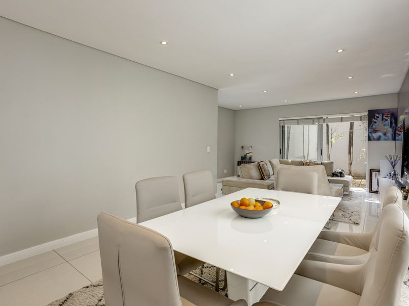 A bright open-plan living and dining area featuring neutral tiled flooring, recessed downlighting, and large sliding glass doors leading to an outdoor space.