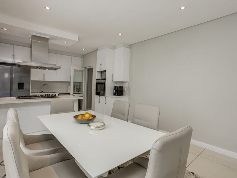 Modern open-plan kitchen and dining area featuring sleek white cabinetry, integrated appliances, a gas hob, and recessed ceiling lighting.