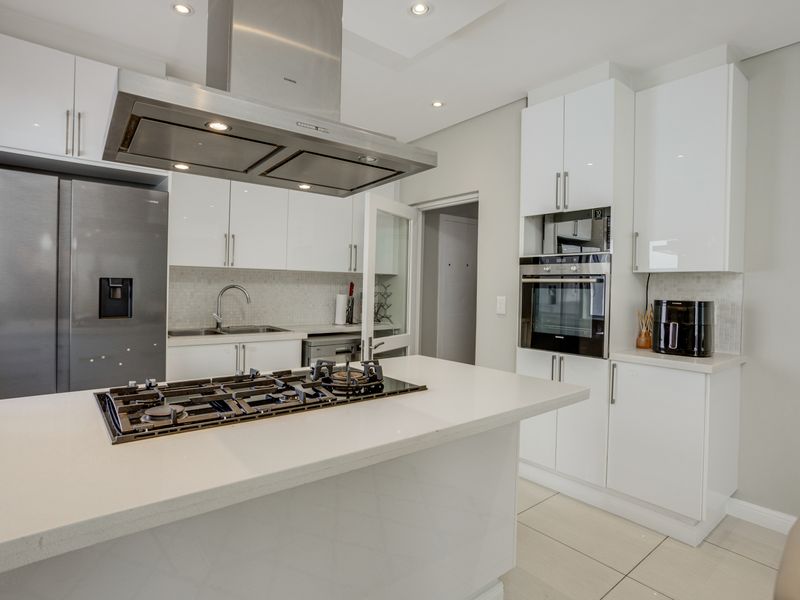 Modern kitchen featuring white cabinetry, stone countertops, a central island with a gas hob, stainless steel extractor fan, and built-in oven.