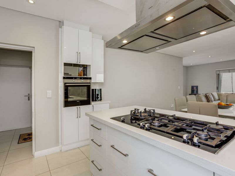 Modern open-plan kitchen featuring a central island with a built-in gas hob, overhead extractor fan, and sleek white cabinetry.