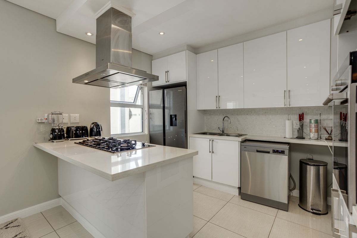 Modern kitchen featuring high-gloss white cabinetry, stone countertops, a central island with a gas hob, stainless steel extractor fan, and integrated dishwasher.