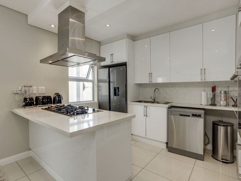 Modern kitchen featuring high-gloss white cabinetry, stone countertops, a central island with a gas hob, stainless steel extractor fan, and integrated dishwasher.