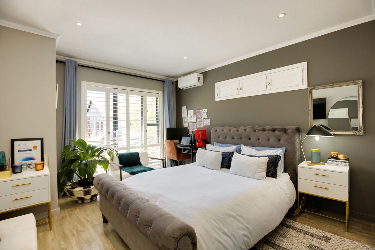 A well-maintained bedroom featuring wood-look flooring, recessed ceiling lighting, a wall-mounted air conditioning unit, and plantation-style shutters on the window.