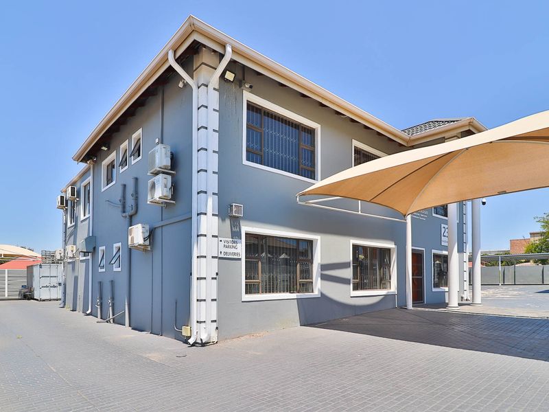 Exterior view of a commercial-style building featuring a paved driveway, shade sail parking area, and multiple wall-mounted air conditioning units.