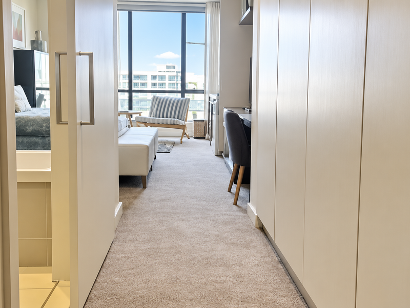 A well-lit bedroom featuring built-in cupboards, carpeted flooring, and large floor-to-ceiling windows offering natural light and a view.