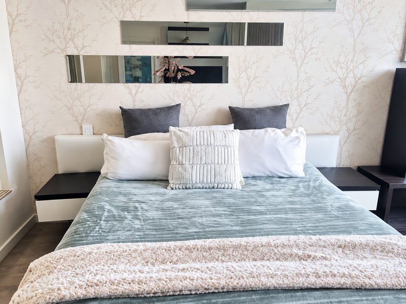 A well-maintained bedroom featuring a built-in headboard with integrated bedside tables and decorative wall mirrors.