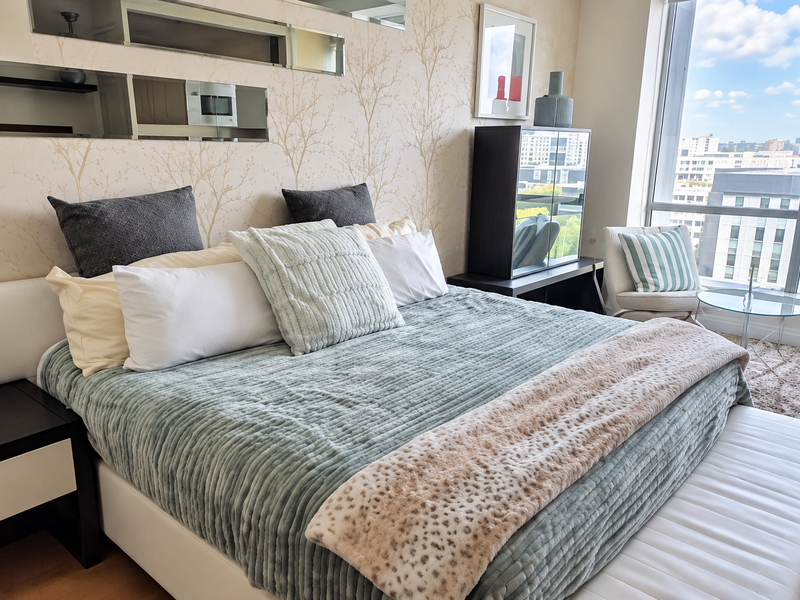 A well-maintained bedroom featuring floor-to-ceiling windows with city views, decorative wallpaper, and integrated wall mirrors.