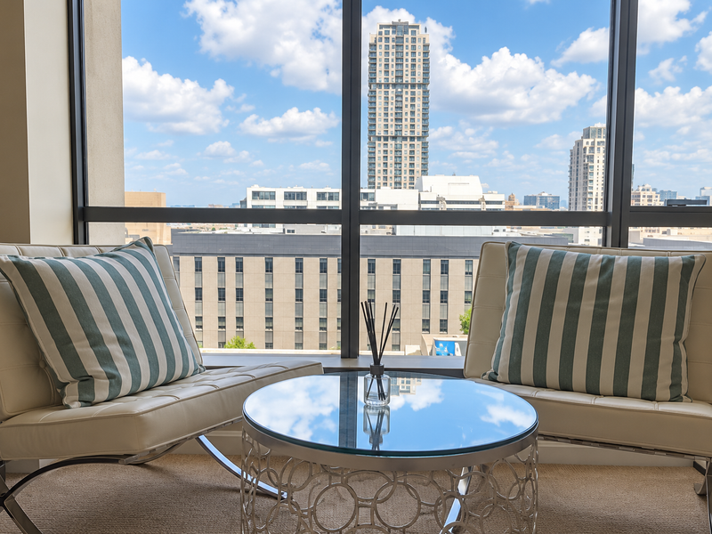A bright living area featuring large floor-to-ceiling windows that provide an expansive urban city view.