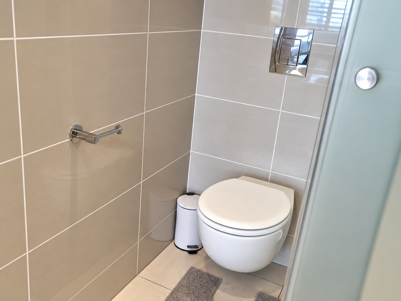 A modern bathroom featuring a wall-mounted toilet with a concealed cistern and neutral-toned ceramic wall tiling.