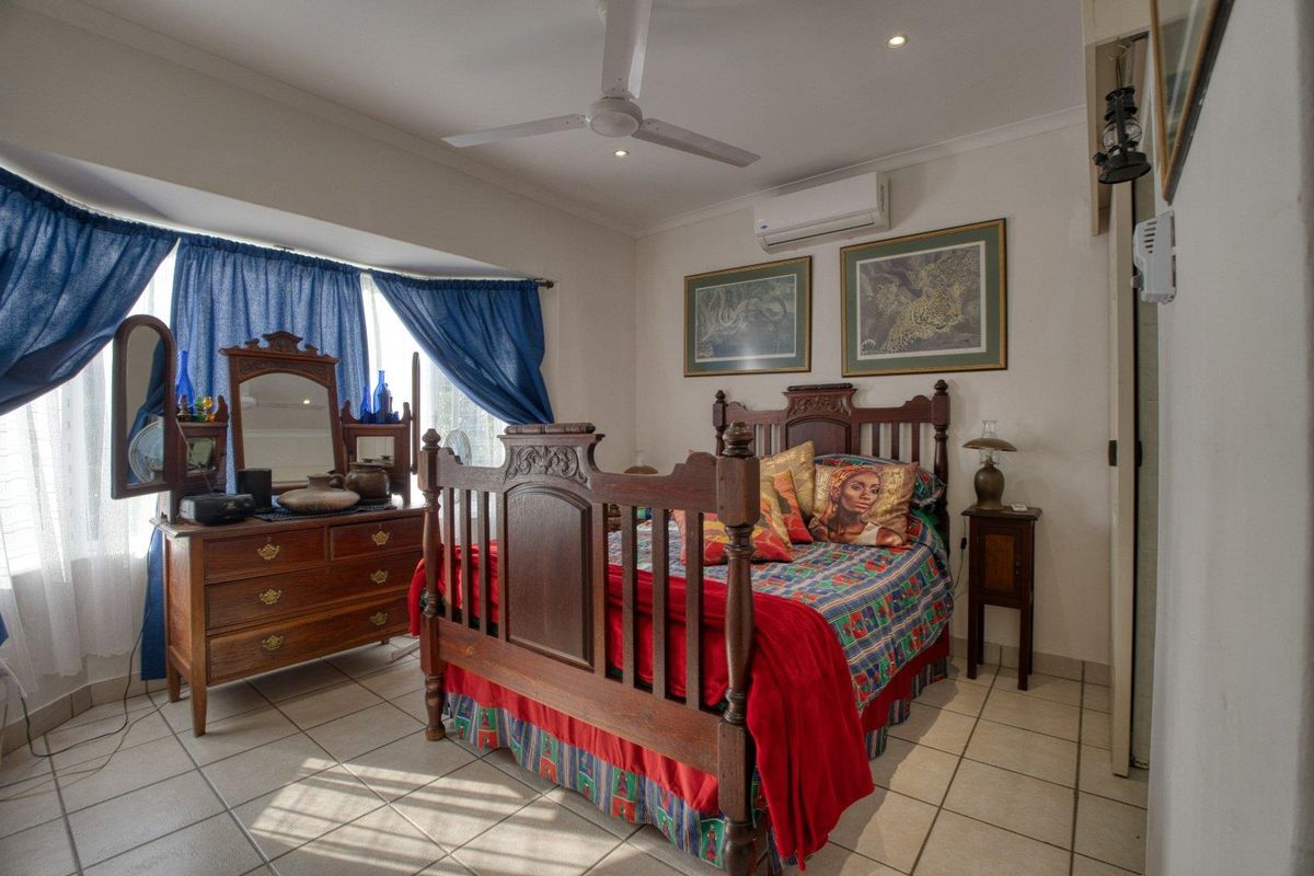 A well-lit bedroom featuring tiled flooring, a ceiling fan, and a wall-mounted air conditioning unit.