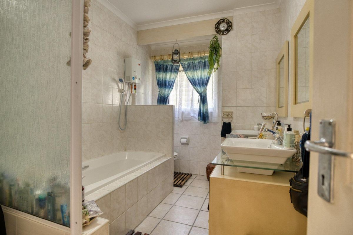 A functional bathroom featuring a built-in bathtub, wall-mounted shower unit, and a vanity basin with tiled flooring and wall finishes.