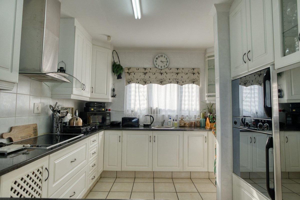 A functional kitchen featuring white cabinetry, dark granite countertops, a built-in oven, and a stainless steel extractor fan with tiled flooring.