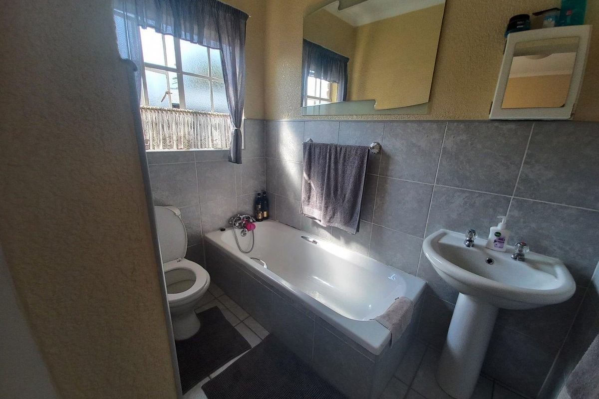 A functional bathroom featuring a bathtub, pedestal basin, and toilet with tiled walls and flooring.