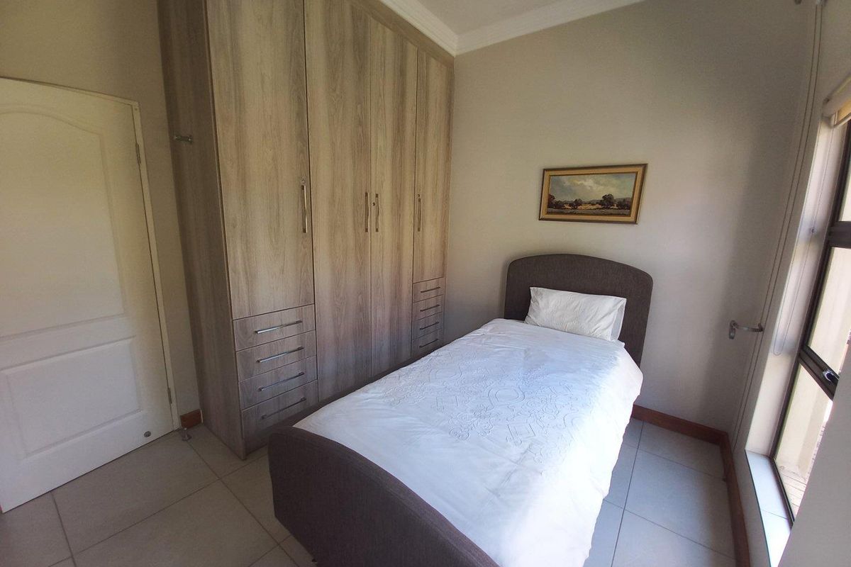 A well-maintained bedroom featuring light wood-grain built-in cupboards, tiled flooring, and large windows providing natural light.