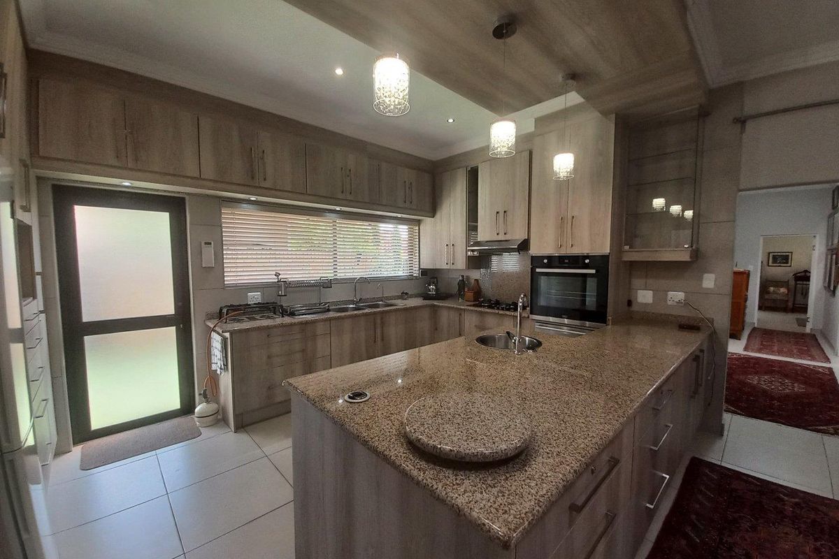 Modern kitchen featuring granite countertops, built-in oven, extractor fan, double sink, and ample cabinetry with integrated lighting and tiled flooring.