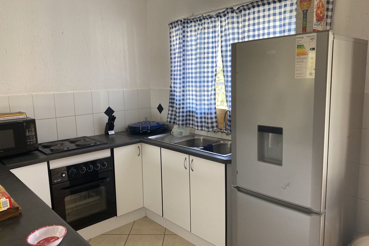 A functional kitchen featuring built-in cabinetry, an electric hob, an oven, and a double sink with tiled backsplash and flooring.