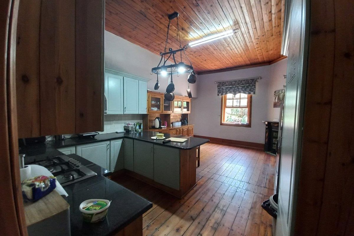 A spacious kitchen featuring timber ceilings, wooden flooring, dark stone countertops, and a central island with integrated cabinetry.