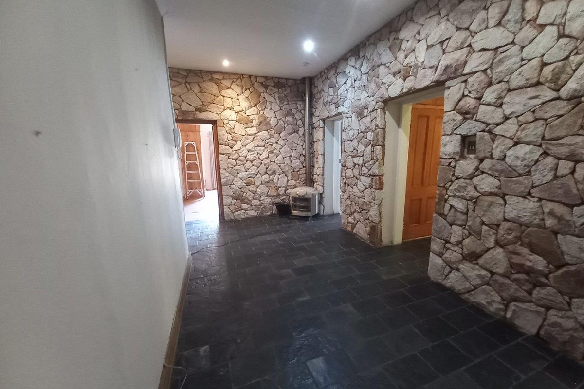 A spacious interior area featuring distinctive natural stone feature walls, dark slate flooring, and recessed downlighting, providing a rustic and textured aesthetic.