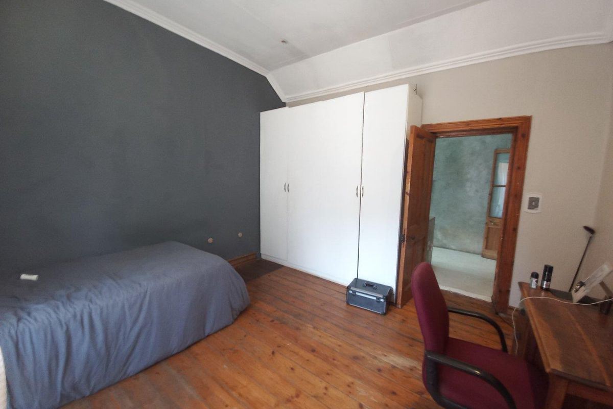 A bedroom featuring original timber flooring, built-in white cabinetry, and a vaulted ceiling with a dark accent wall.