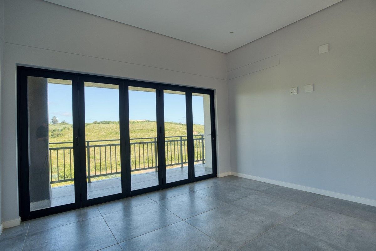 A bright, modern living area featuring large black-framed folding glass doors that open onto a balcony with scenic hillside views.